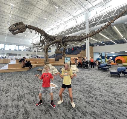 2 children standing in front of a dinosaur in a museum