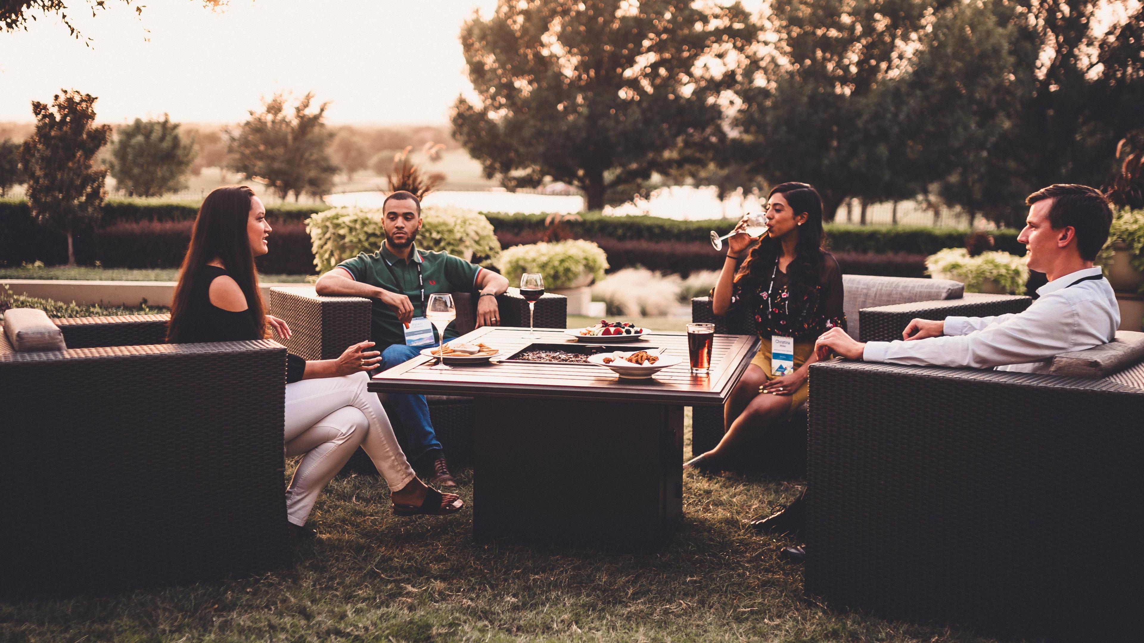 Four people sitting on some outdoor furniture having a some drinks