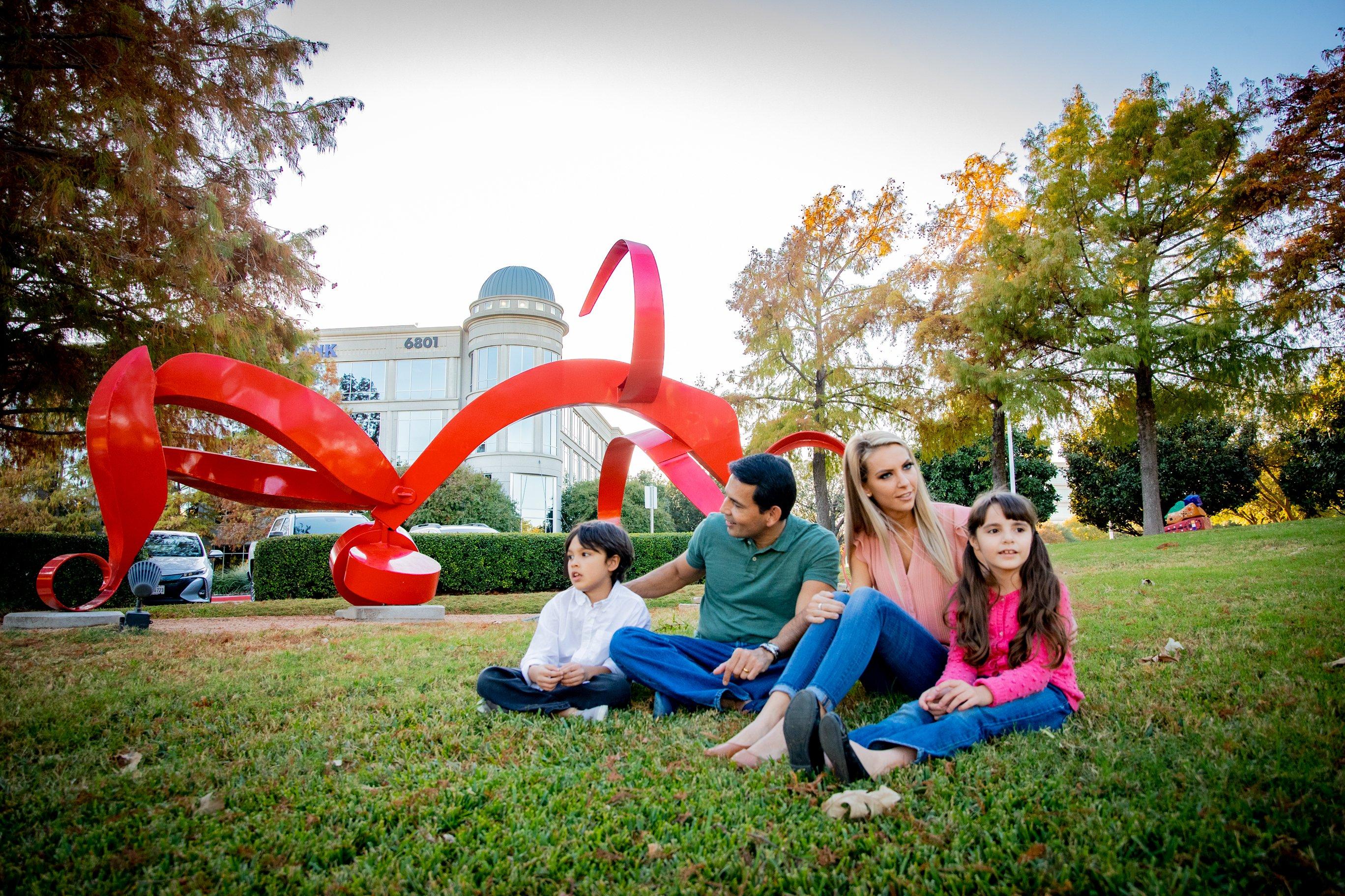 Family sitting on the lawn in front of a big red statue