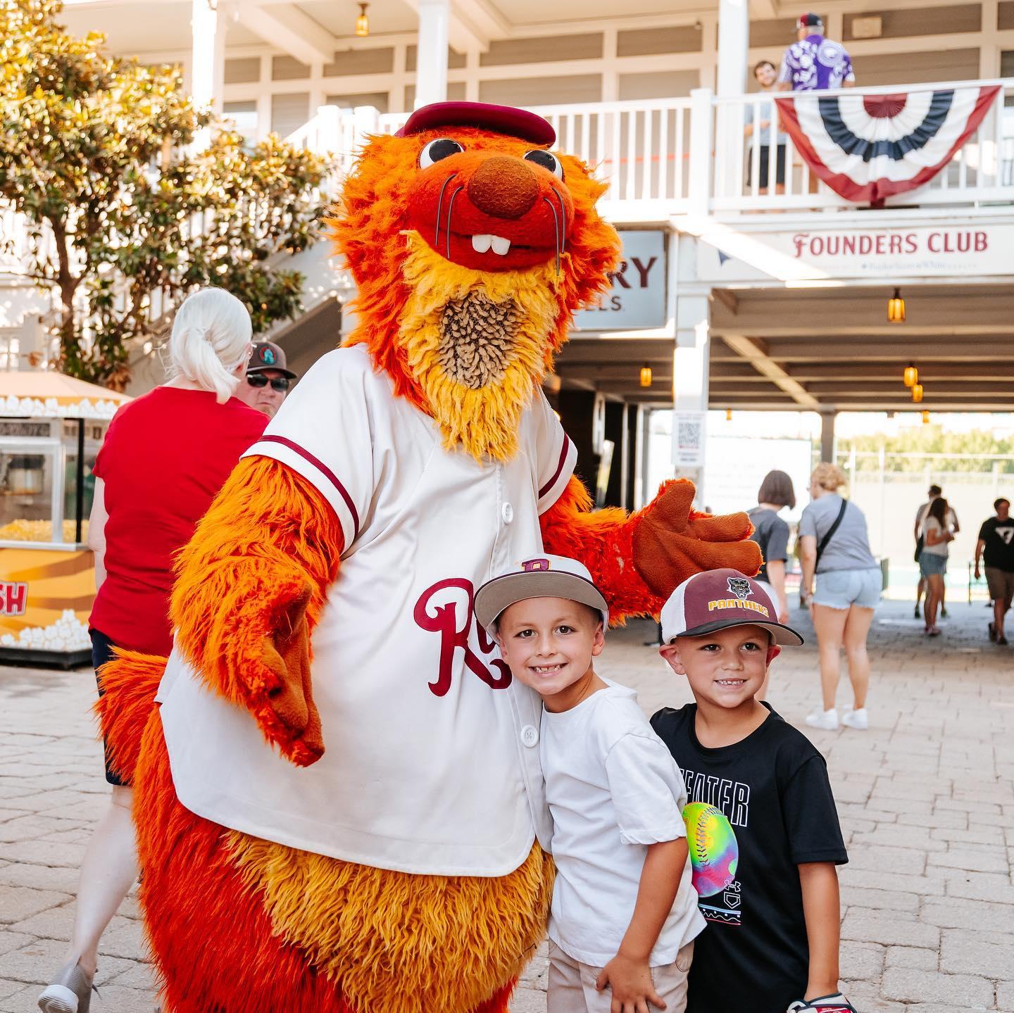 Two young boys pose for a photo with a large orange sports mascot.