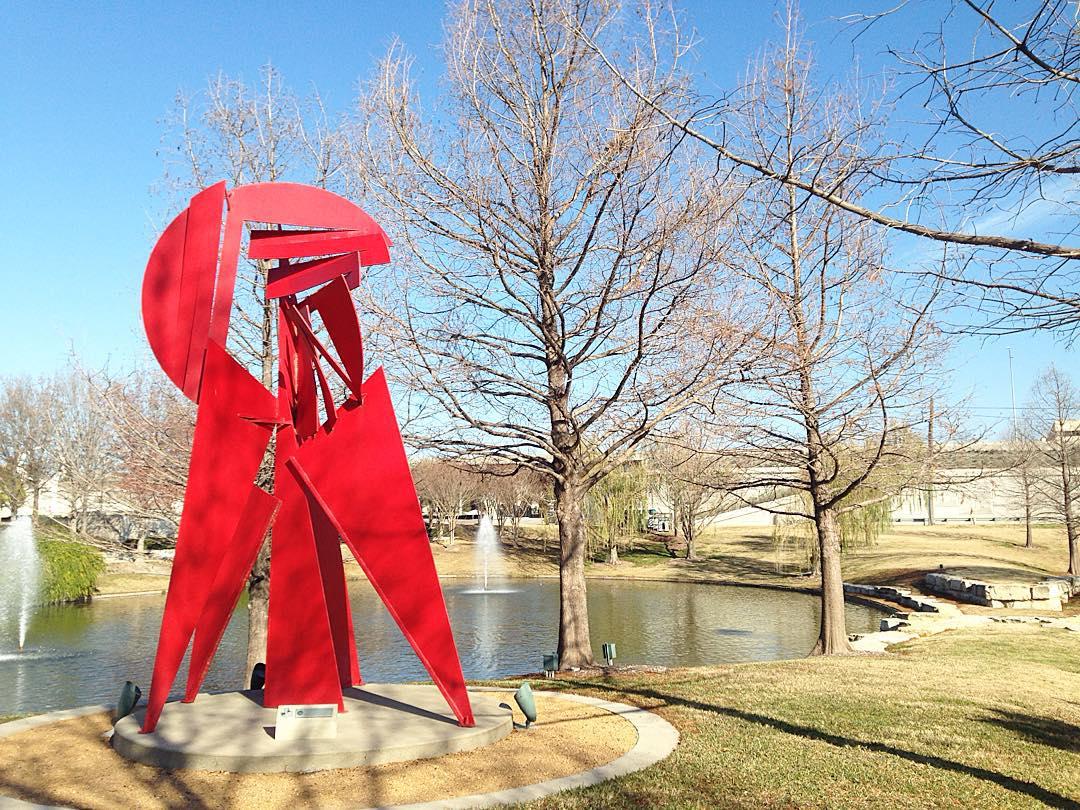 red metal sculpture in a park by a lake