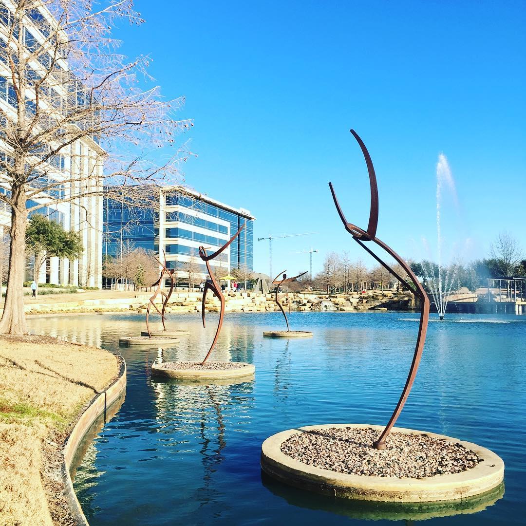 metal sculpture that look like people dancing on rocky islands in the lake